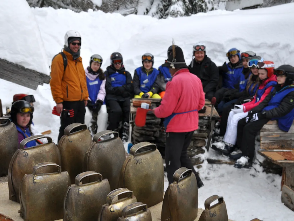 Gruppe sitzt an einem Tisch vor der Hütte, davor Kuhglocken.